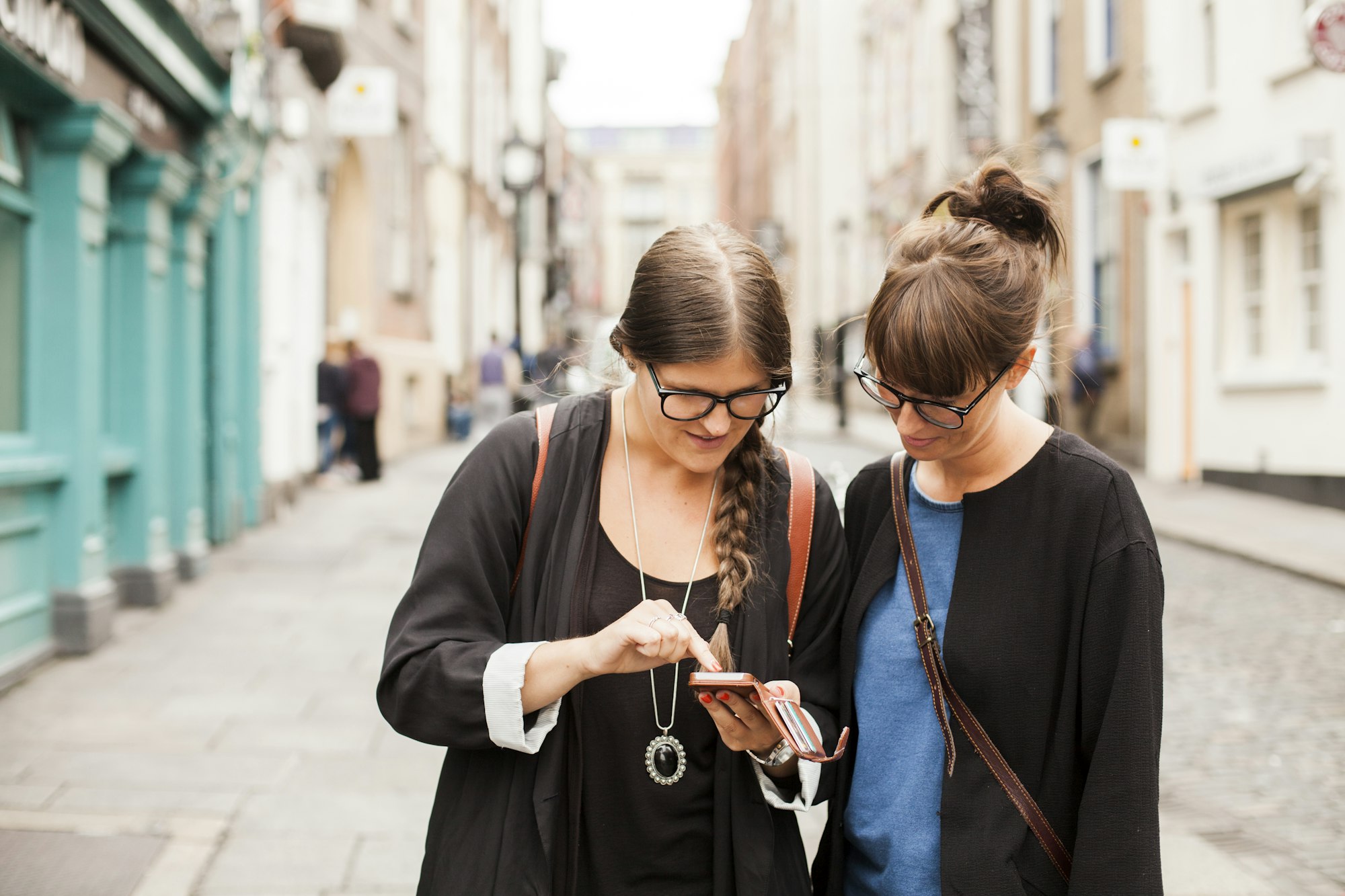 Female friends using smart phone on city street